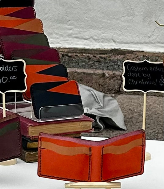 A partial shot of a market stand showing cardholders on a verticle display and a wallet. All items are make from brightly colored leathers 