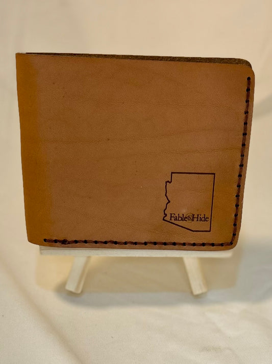 Outside of a tan wallet. There is an outline of the state of Arizona in the bottom right corner with the Fable&Hide makers mark inside the outline 