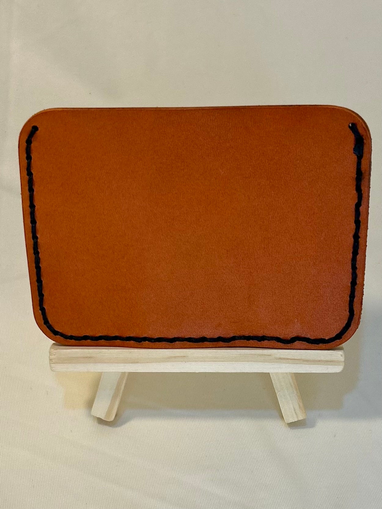 Orange back of a card holder wallet with black stitching. The stitching is imperfect 