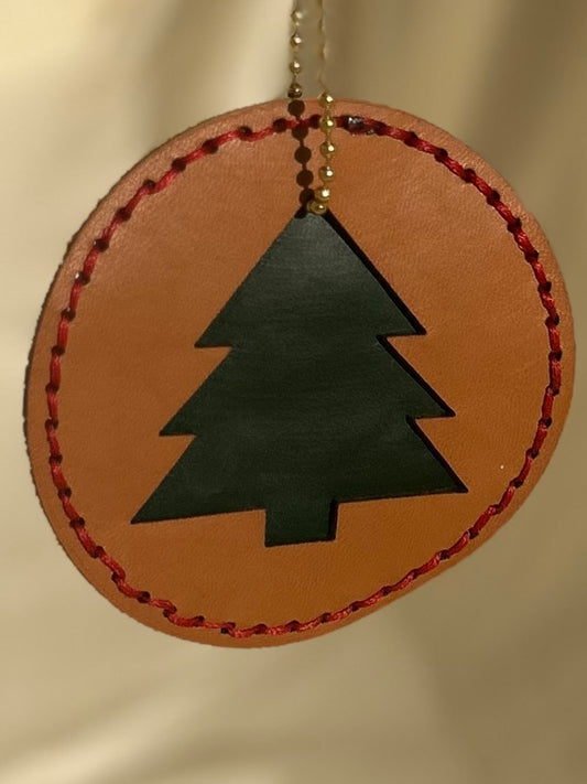 Tan circular ornament with a green tree cut out in the middle and red stitching on the outside 