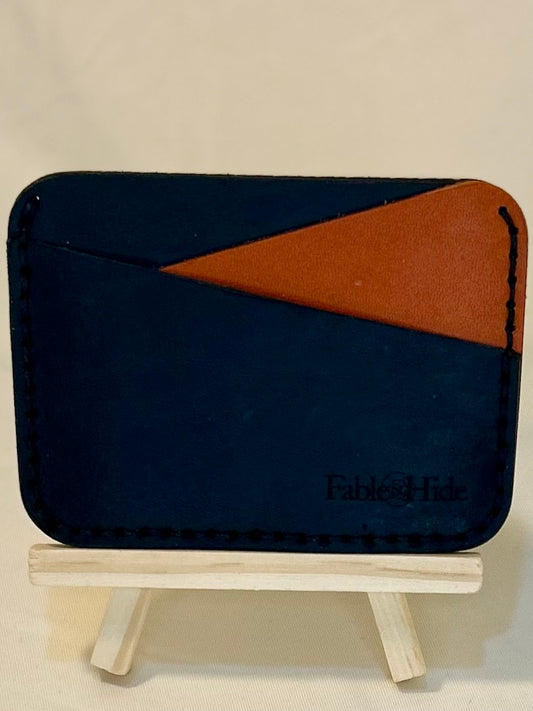 A black card holder wallet with an orange card slot pocket. Stitching is in black and there is a fable&Hide makers mark in the bottom right corner. 