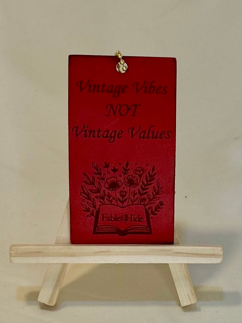 Red rectangle leather charm with gold ball chain. The charm says “Vintage Vibes NOT Vintage Values” and has an open book with flowers image with the Fable&Hide makers mark on the book pages 