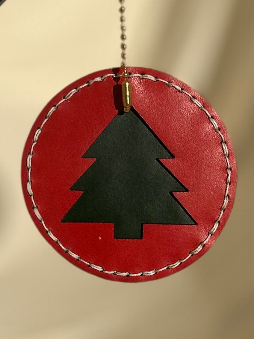 Red circular ornament with a green tree cut out in the middle and white stitching on the outside 