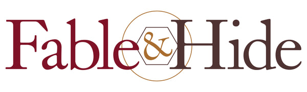 Fable&Hide logo. Fable is in maroon, & is in gold and surrounded by a hexagon and a circle, hide is in brown