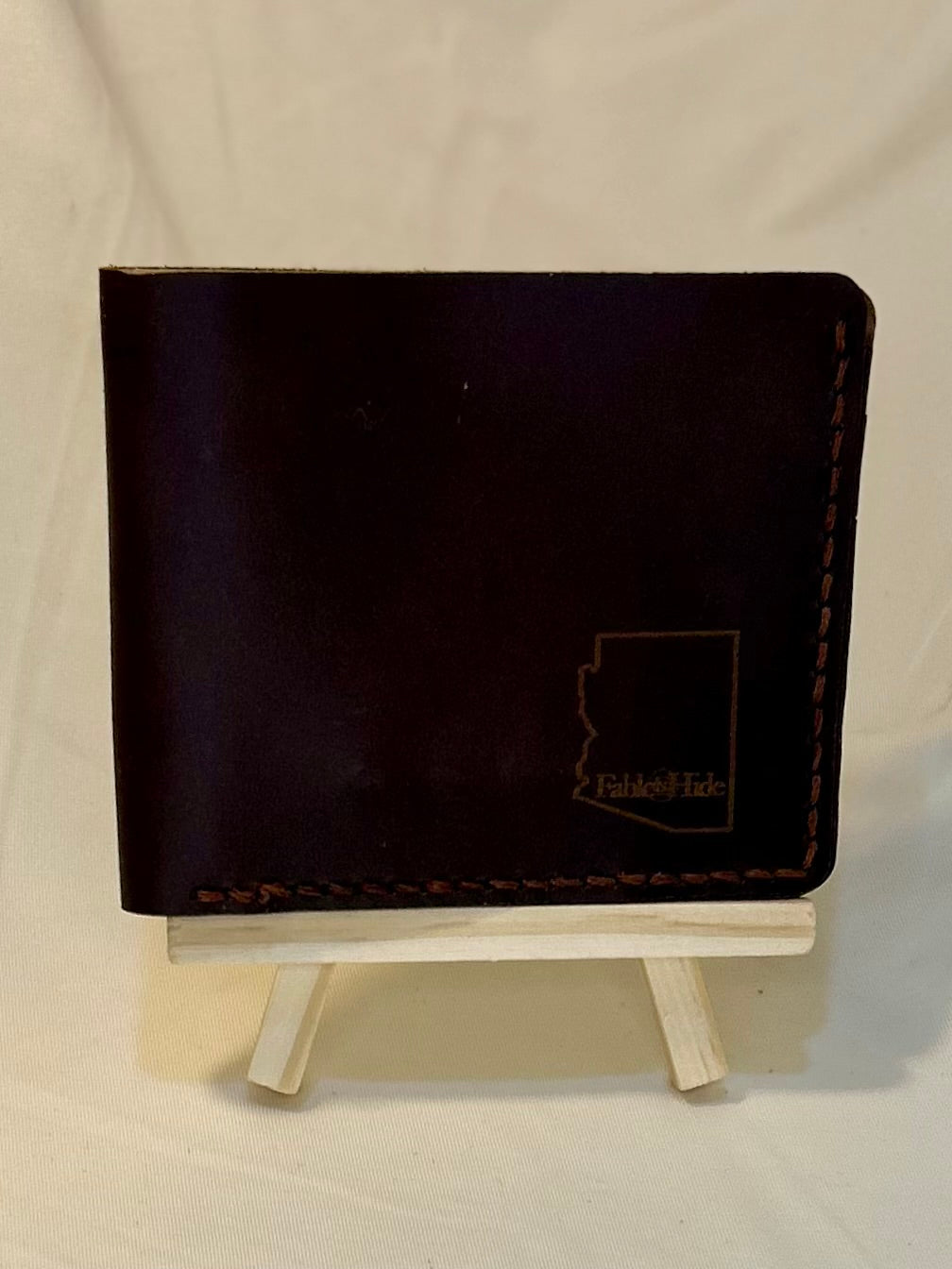 Dark brown wallet with the outline of the state of Arizona in the bottom right corner and a fable and hide makers mark inside it