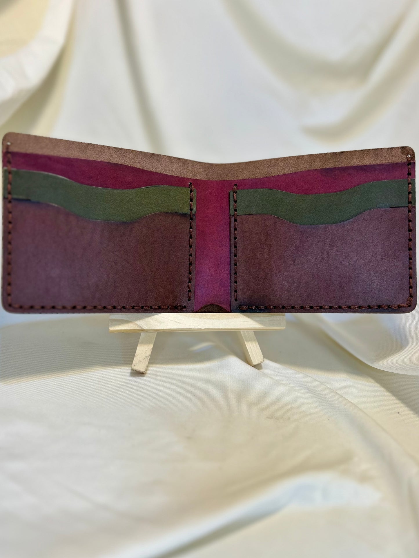 A wallet in brown, maroon, and green. It’s a billfold style wallet. It has two card holders on each side and a money pocket in the back. 